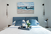 Bed with blue and white bed linen and seascape in modern bedroom