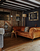 Living room with cognac-coloured velvet sofa, wooden floor and brick wall