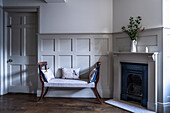 Bench with decorative cushions next to a fireplace in a wood-panelled living room