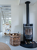 Black wood-burning stove next to wicker basket with logs in bright living room