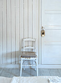 White-painted wooden chair with seat cushion in front of country-style wood paneling