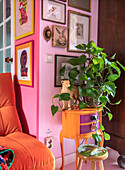 Orange side table with houseplant in front of colorful picture wall