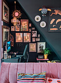 Dark desk area under the stairs with picture wall and pink sofa in the foreground