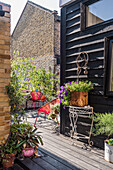 Wooden terrace with red chairs, flower pots and black wooden facade in the backyard