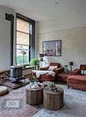 Sitting area with red velvet armchairs, wood-burning stove, round wooden tables and plants in the living room