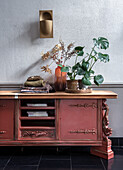 Rotes Vintage-Sideboard mit Pflanzen und Trockenblumenarrangement vor strukturierter Wand