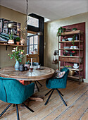 Dining area with antique, round wooden table, turquoise-coloured chairs and wooden shelf