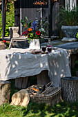 Rustikaler Gartentisch mit Leinentischdecke und Blumenvase, umgeben von Baumstumpfhockern