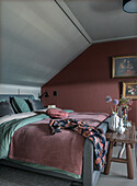 Bedroom with sloped ceiling, red accent wall and wooden table with flower vases