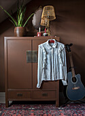 Brown wardrobe with retro table lamp, white blouse and guitar