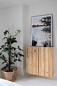 Floating pine cupboard with framed landscape painting and houseplant in basket