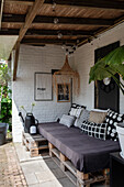 Covered outdoor seating area with pallet bench, patterned pillows and hanging raffia lamp