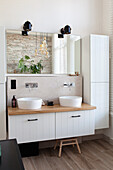 Modern bathroom with double washbasin on wooden countertop and white cabinets