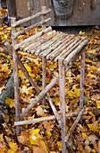 DIY-Hocker aus Holzästen auf herbstbelaubtem Boden