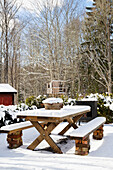 Schneebedeckter rustikaler Holztisch im winterlichen Garten