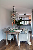 Set wooden dining table with fabric chairs and chandelier with kitchen in the background