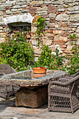 Naturstein-Tisch mit Korbsesseln vor einer Backsteinmauer im Garten