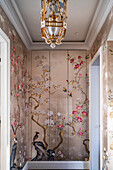 Gilded chandelier above hand-painted chinoiserie wallpaper mural with floral pattern