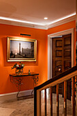 Orangefarben gestrichener Flur mit Holztür und beleuchtetem Gemälde