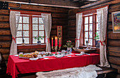 Table setting in rustic wooden hut with red tablecloth and candlestick