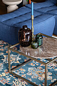 Round marble table with glass vases on an oriental rug in front of a blue sofa