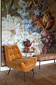 Ochre-colored upholstered armchair in front of large-scale wall art with floral pattern in the living room