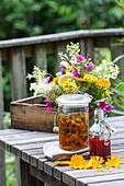 Herbal oil, syrup and bouquet of flowers on a wooden table in the garden