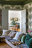 Patterned wallpaper with palm trees and zebra corner sofa in living room with view into dining room