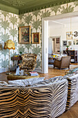 Living room with zebra pattern sofa, palm pattern wallpaper and baroque fabric armchair