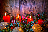 Vier rote Kerzen auf Adventsgesteck, drei Kerzen brennend