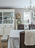 Dining room with white display cabinet and chandelier, table with embroidered tablecloth