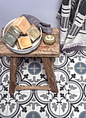 Rustic wooden stool with bowl and soaps on a patterned tiled floor