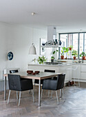 Dining area with black leather chairs, square wooden table and open-plan kitchen