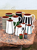 Ceramic jugs and mugs with hand-painted patterns on an outdoor stone table