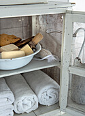 White wooden cabinet with towels and soaps in a tin bowl