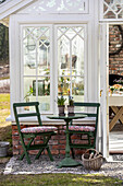 Cosy seating area with green metal table and chairs in front of greenhouse