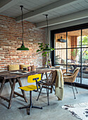 Dining room with rustic wooden table, yellow chair and industrial lamps in front of brick wall