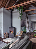 Cozy living room with wood-burning stove, rattan chair and grey couch under ceiling beams