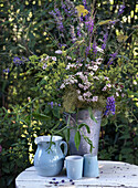 Bouquet of flowers in zinc vase next to blue ceramic crockery on garden table