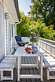 Gedeckter Holztisch mit Erdbeeren, Erfrischungsgetränk und Lupinen-Strauß auf der Terrasse