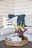 Rattan tray with bouquet of flowers and maritime decoration in front of bench seat