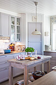 Light-coloured country kitchen with basil pot, bread and candle on kitchen island