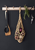 Net with red onions and kitchen utensils on wooden hook rail