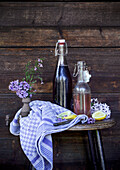 Glass bottles with syrup, lemon slices and lilac flowers on a rustic wooden stool