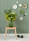 Wooden chair with green bouquet of flowers in front of green wall with decorative plates