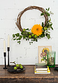 Decorative wreath of twigs and orange-coloured blossom on white brick wall