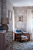 Reading chair with wooden frame next to window in light grey wallpapered room