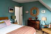 Bedroom with wooden furniture, round wall mirror and green-blue colored walls