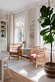 Two rattan armchairs with cushions in a bright living room with floral blinds and large window