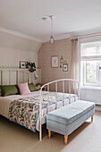 Bedroom with white metal bed, colourful bedspread and upholstered footstool